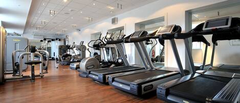 A gym with multiple treadmills, weight machines, and a wooden floor.