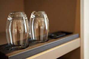 Deux verres transparents sont posés sur une étagère, à côté d’un objet noir.