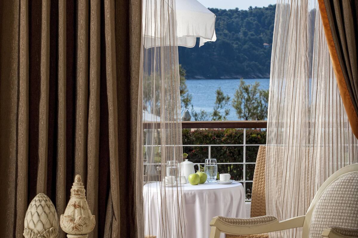 A room with a view of a body of water, a table with a white tablecloth, and a chair.