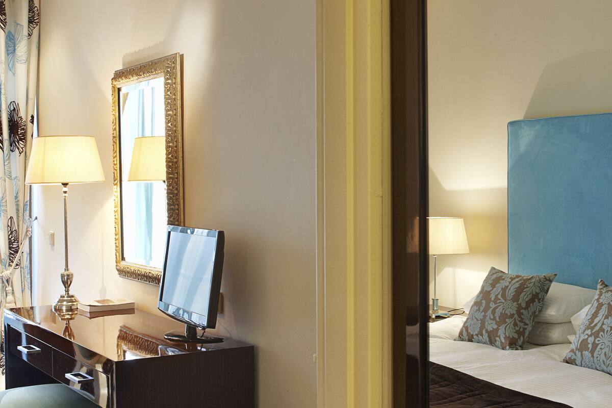 A hotel room with a bed, a desk with a computer, a chair, a lamp, and a mirror.