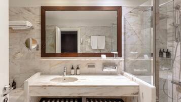 Un baño moderno con lavamanos de mármol, un espejo grande, ducha con mampara de vidrio y un perchero para toallas.