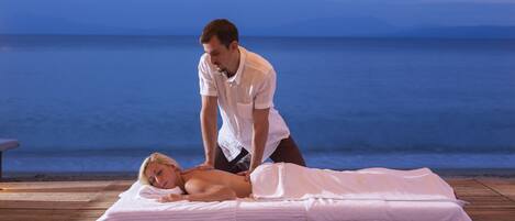 A massage therapy session on a wooden deck by the sea.