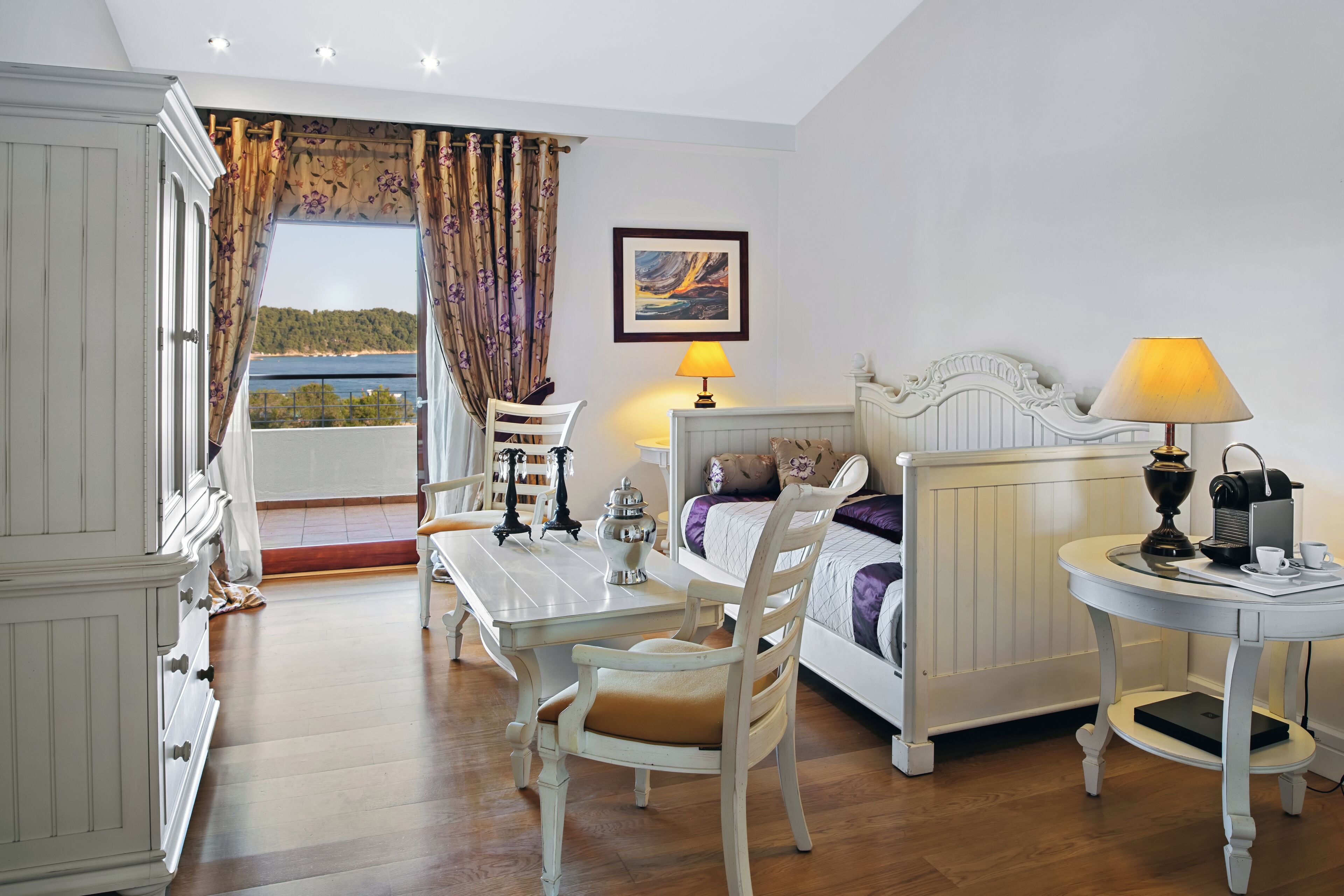 A bedroom with a bed, bedside table, lamp, and a view of the outdoors.