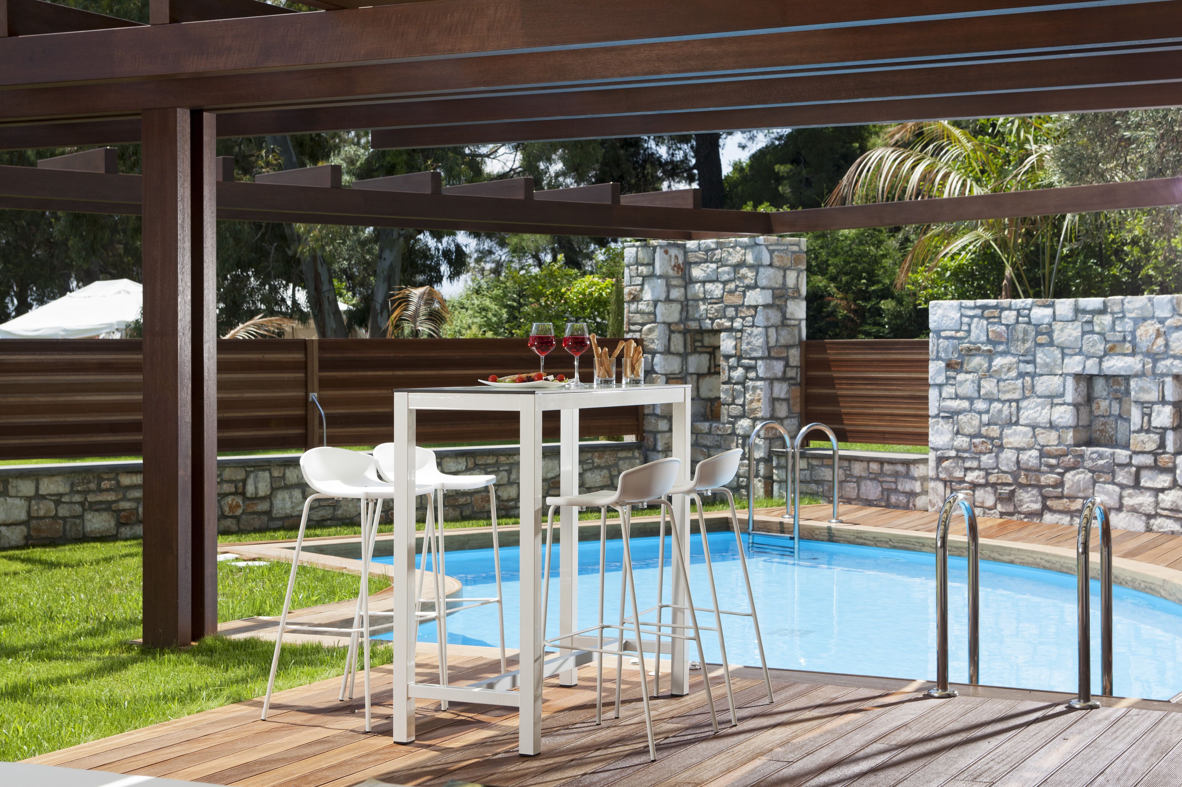 A poolside area with a table and chairs, a stone wall, and a wooden deck.