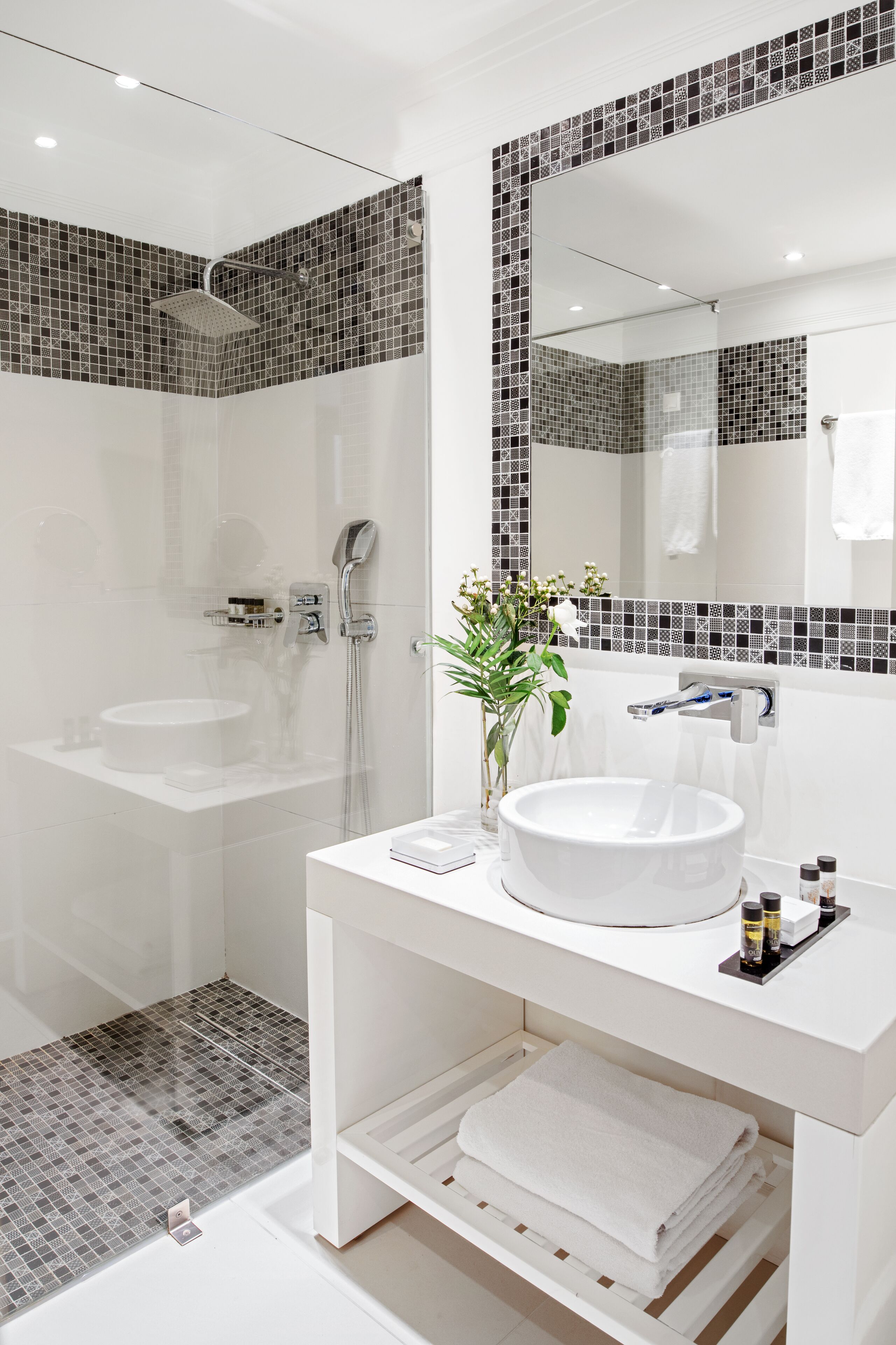 A modern bathroom with a large mirror, white sink, and shower area.