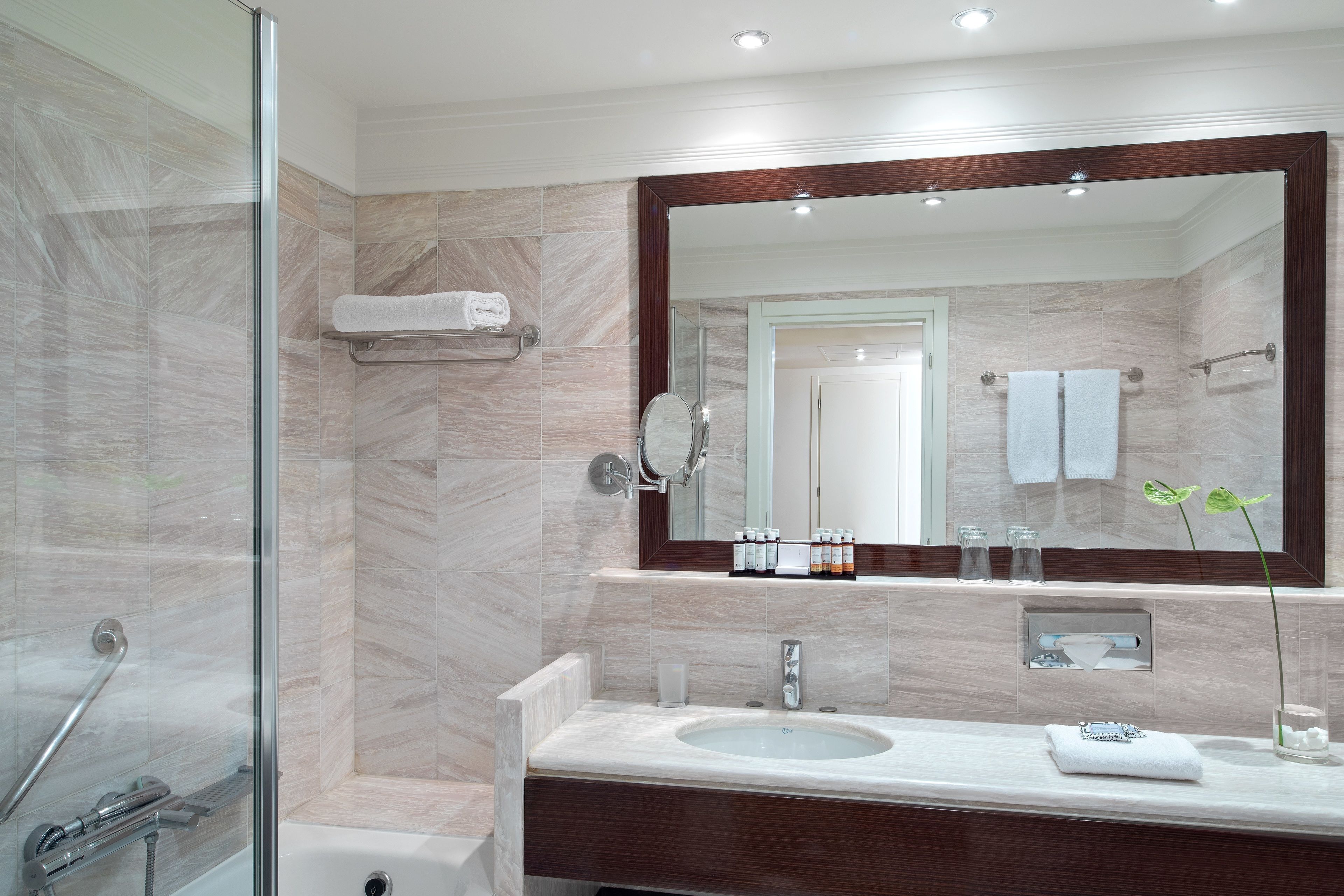 A modern bathroom with a glass shower enclosure, a large mirror, and a vanity with a sink and towel rack.