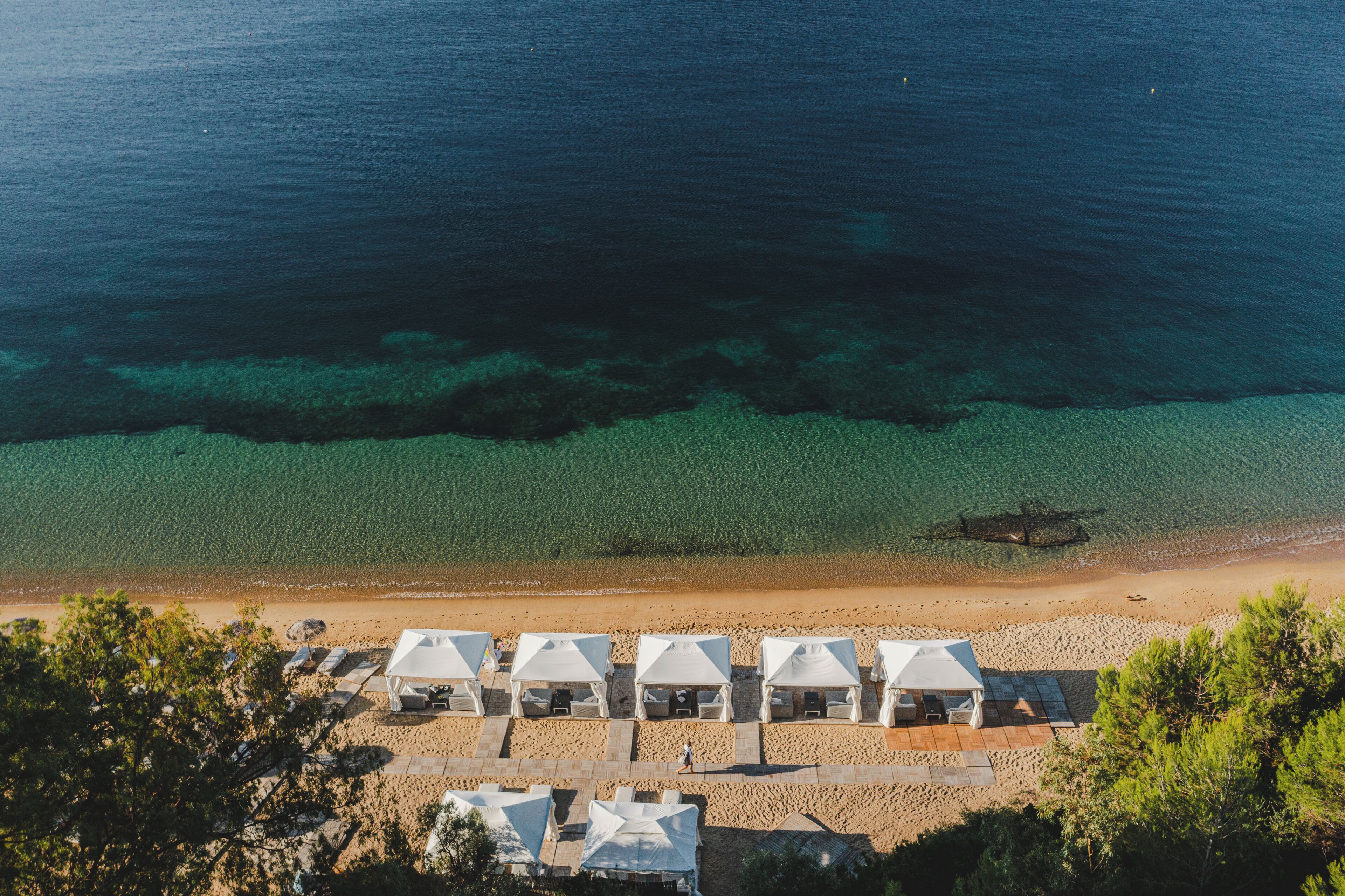 An aerial view of a beach with clear waters and a row of white tents.
