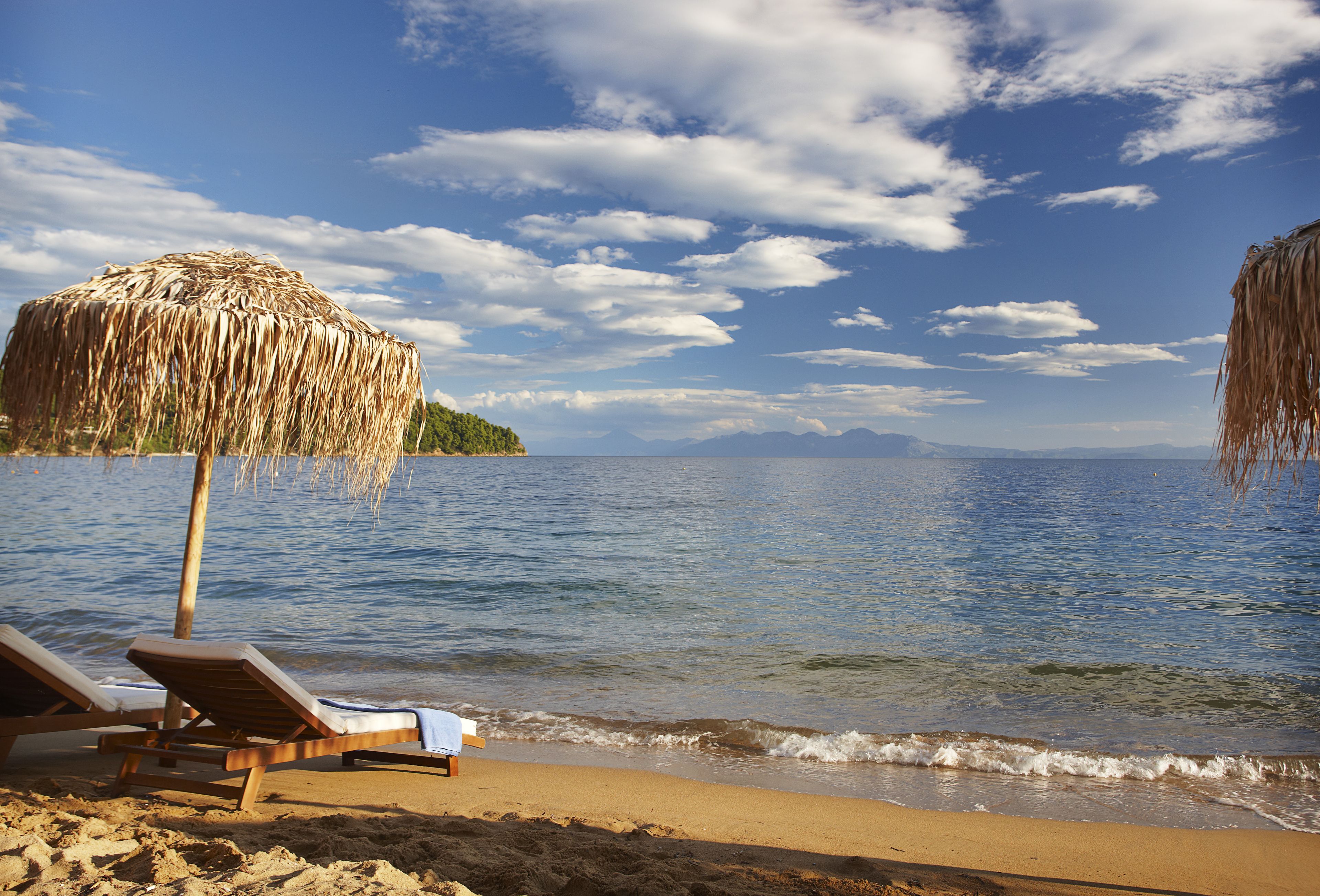 A beach with two lounge chairs and a straw umbrella.