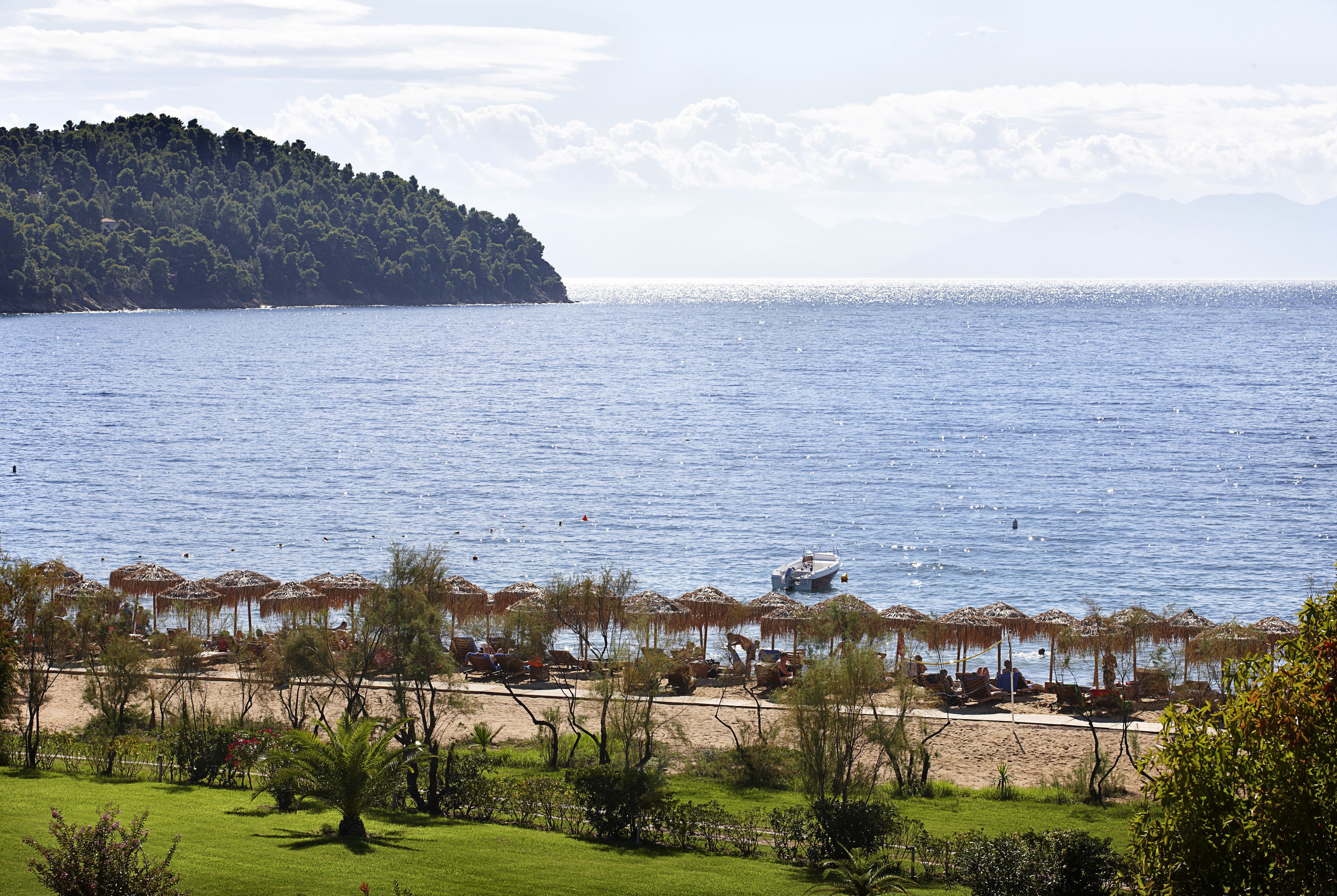 Une plage avec des parasols, un bateau et, au loin, une colline boisée.