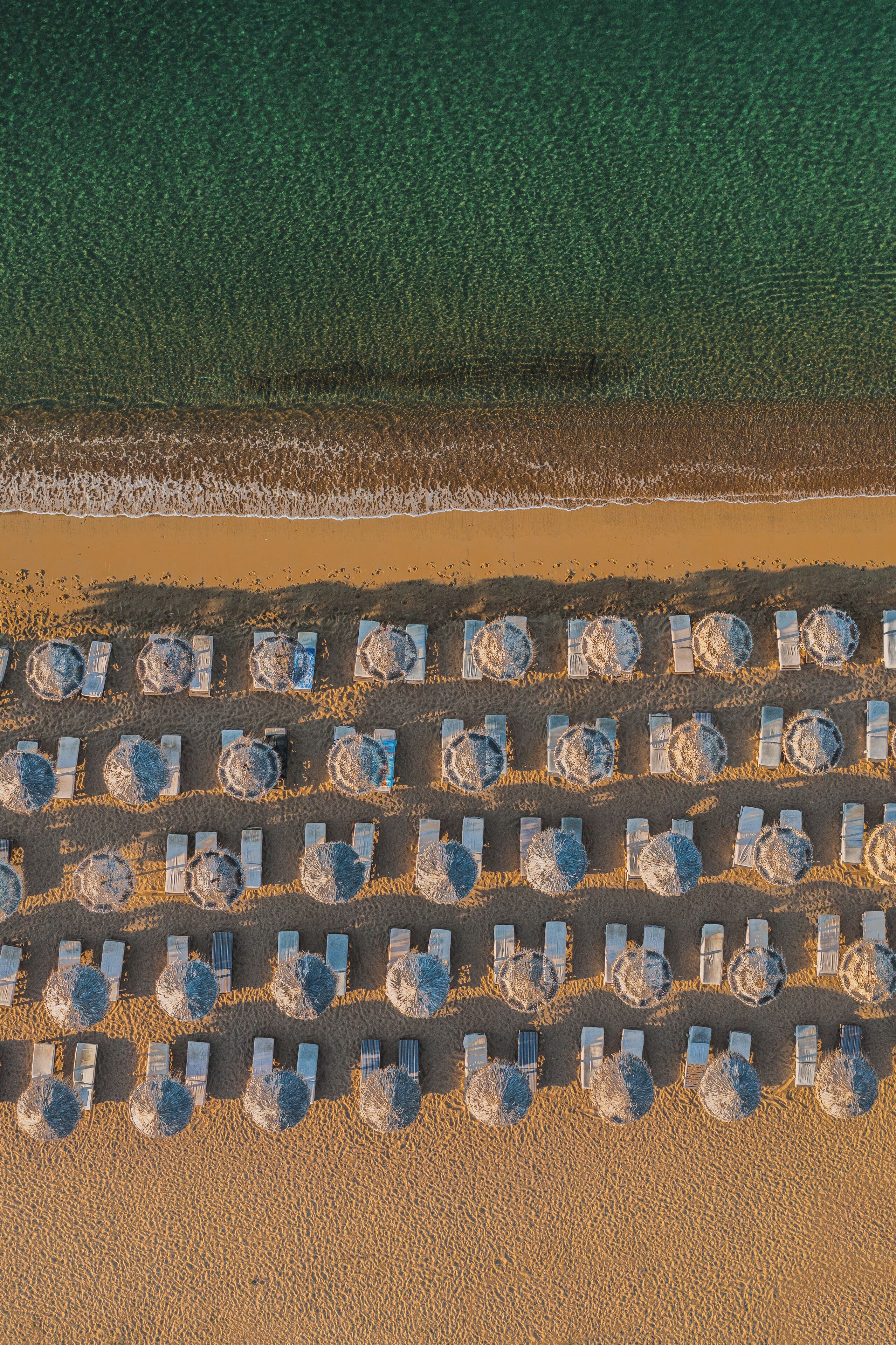 Luchtbeeld van een strand met rijen ligbedden en parasols, netjes gerangschikt.
