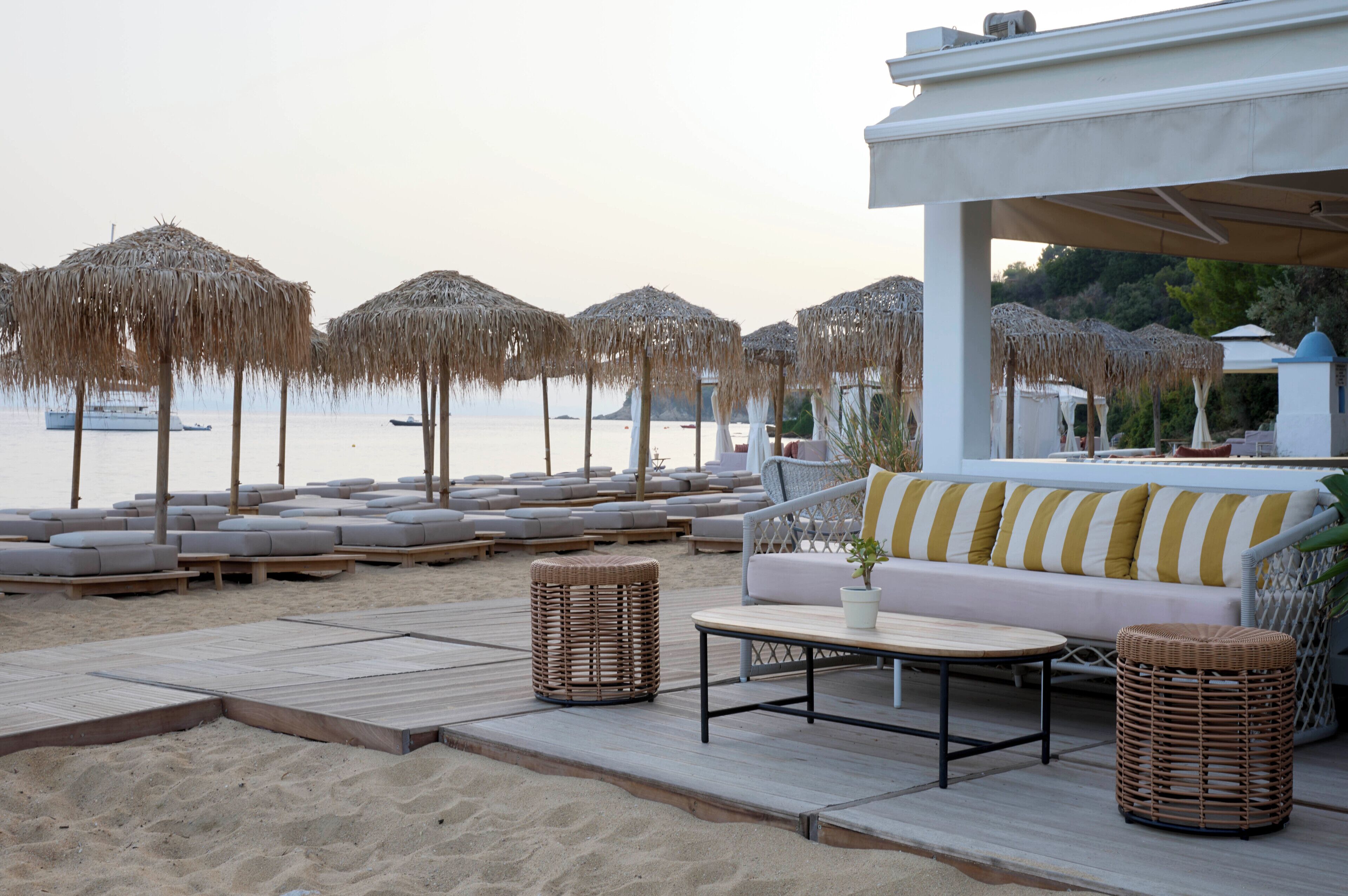 Eine Strandlounge mit Liegestühlen, einer Sitzecke und Reetdach-Sonnenschirmen.
