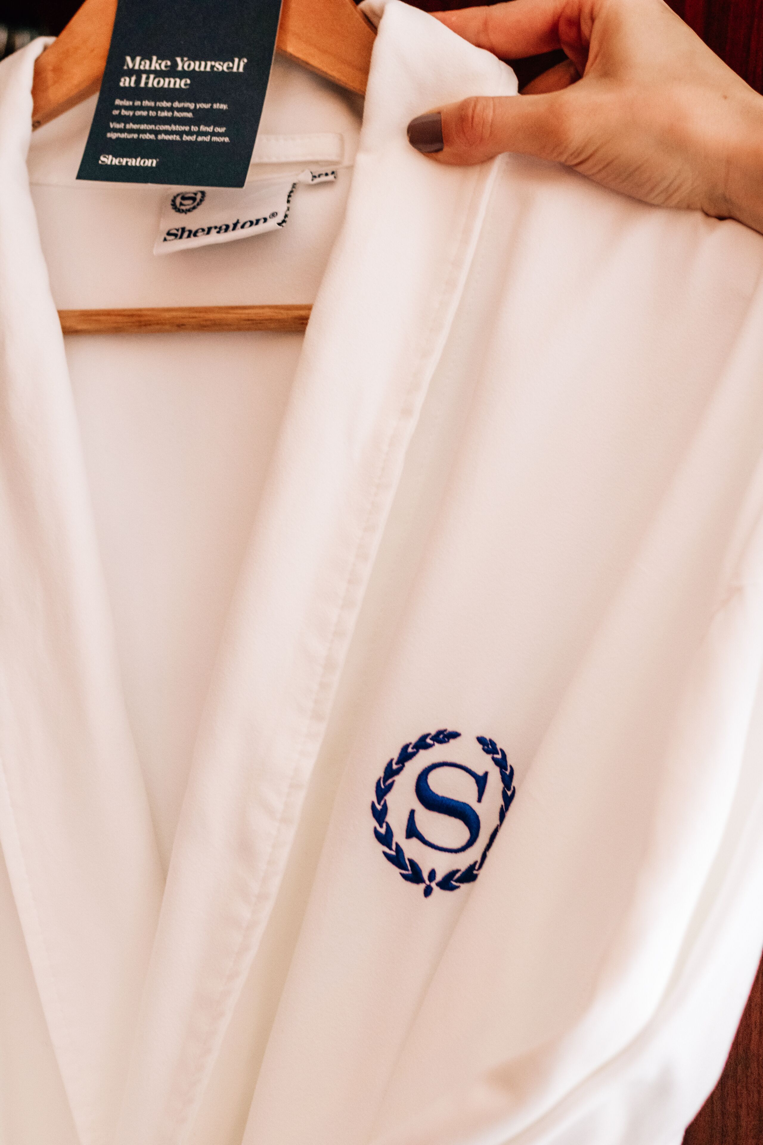 Una bata blanca con logotipo con monograma colgada en una percha de madera.