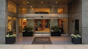 Entree van een Sheraton hotel met een moderne gevel, grote ramen en een gastvrij ontvangstgebied met potplanten.