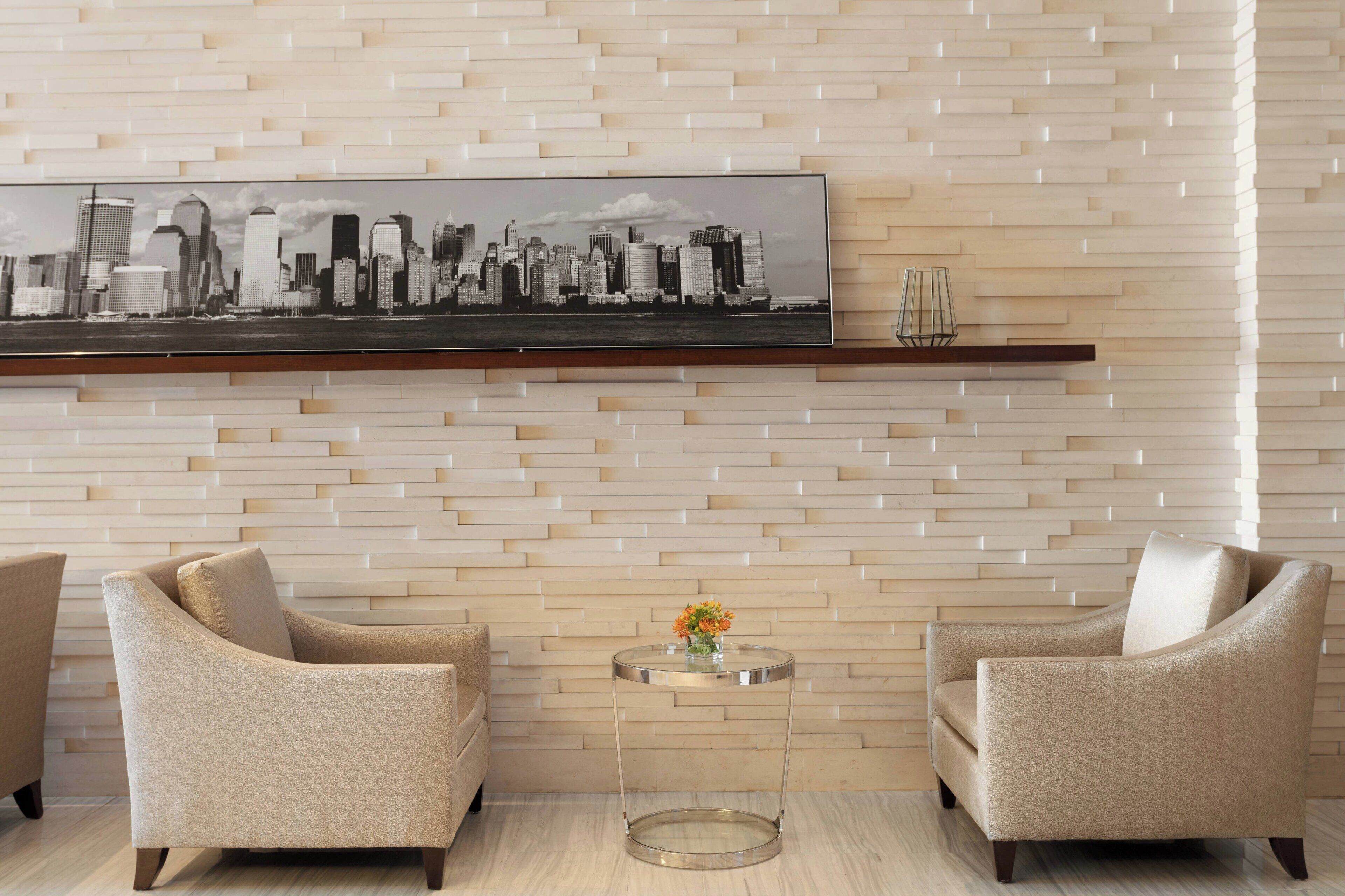 Una habitación moderna con un cuadro de un paisaje urbano, dos sillones beige, una mesita redonda con un florero y suelo de madera.