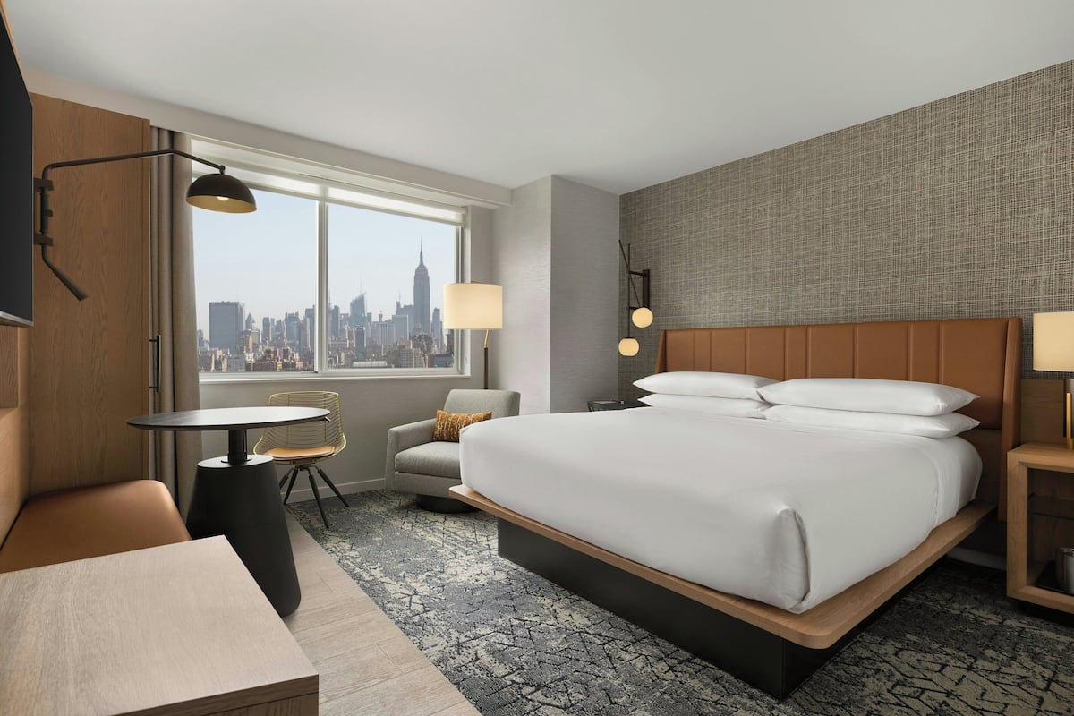 Une chambre d’hôtel avec un grand lit, un bureau, une chaise et une vue sur le panorama urbain.