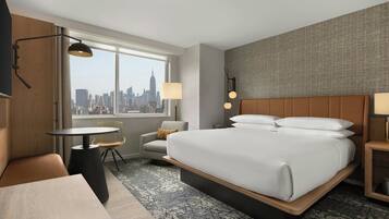 A hotel room with a large bed, a desk, a chair, and a view of a city skyline.