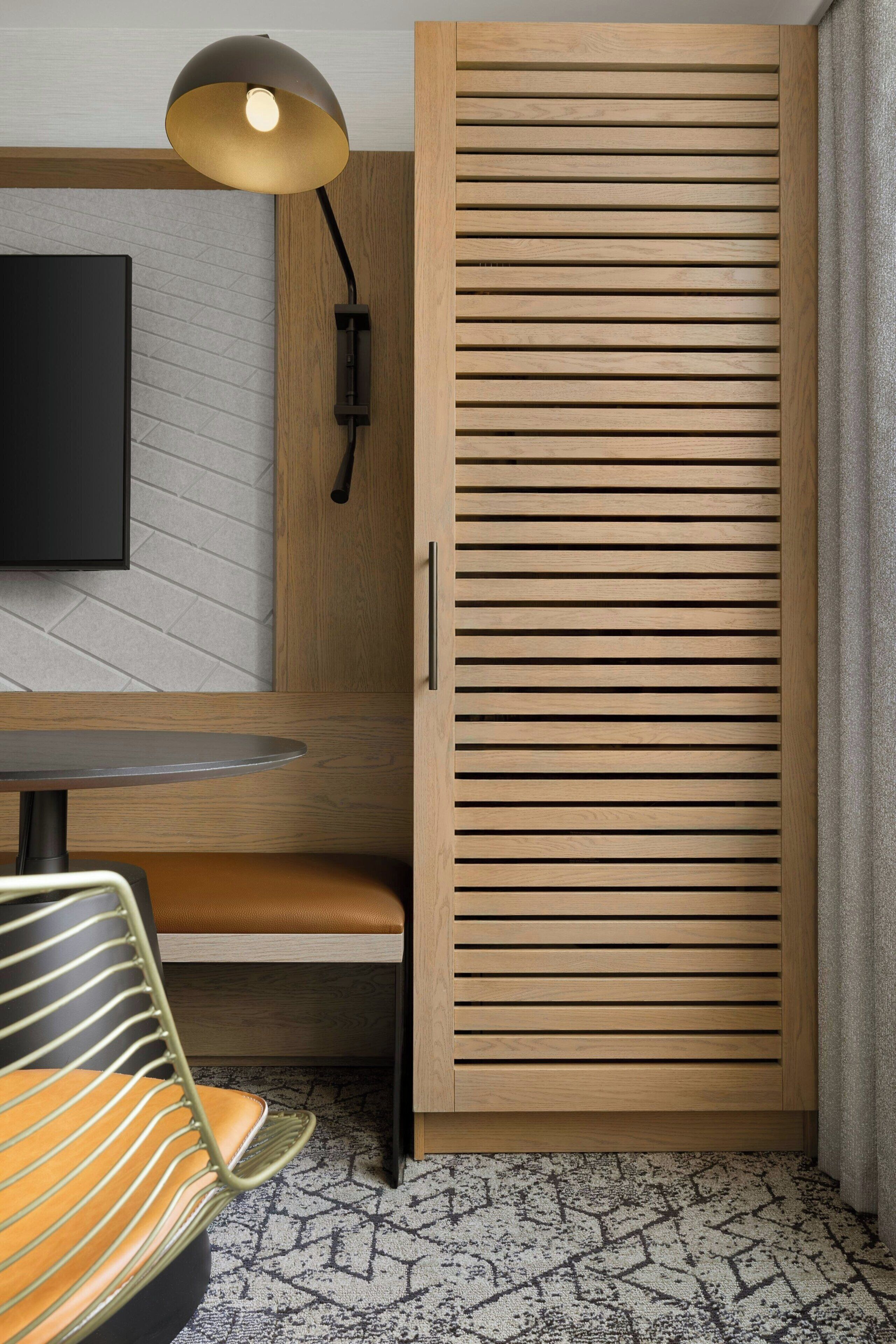 Une pièce comprenant une armoire en bois, une table ronde, une chaise, un téléviseur fixé au mur et un lampadaire.