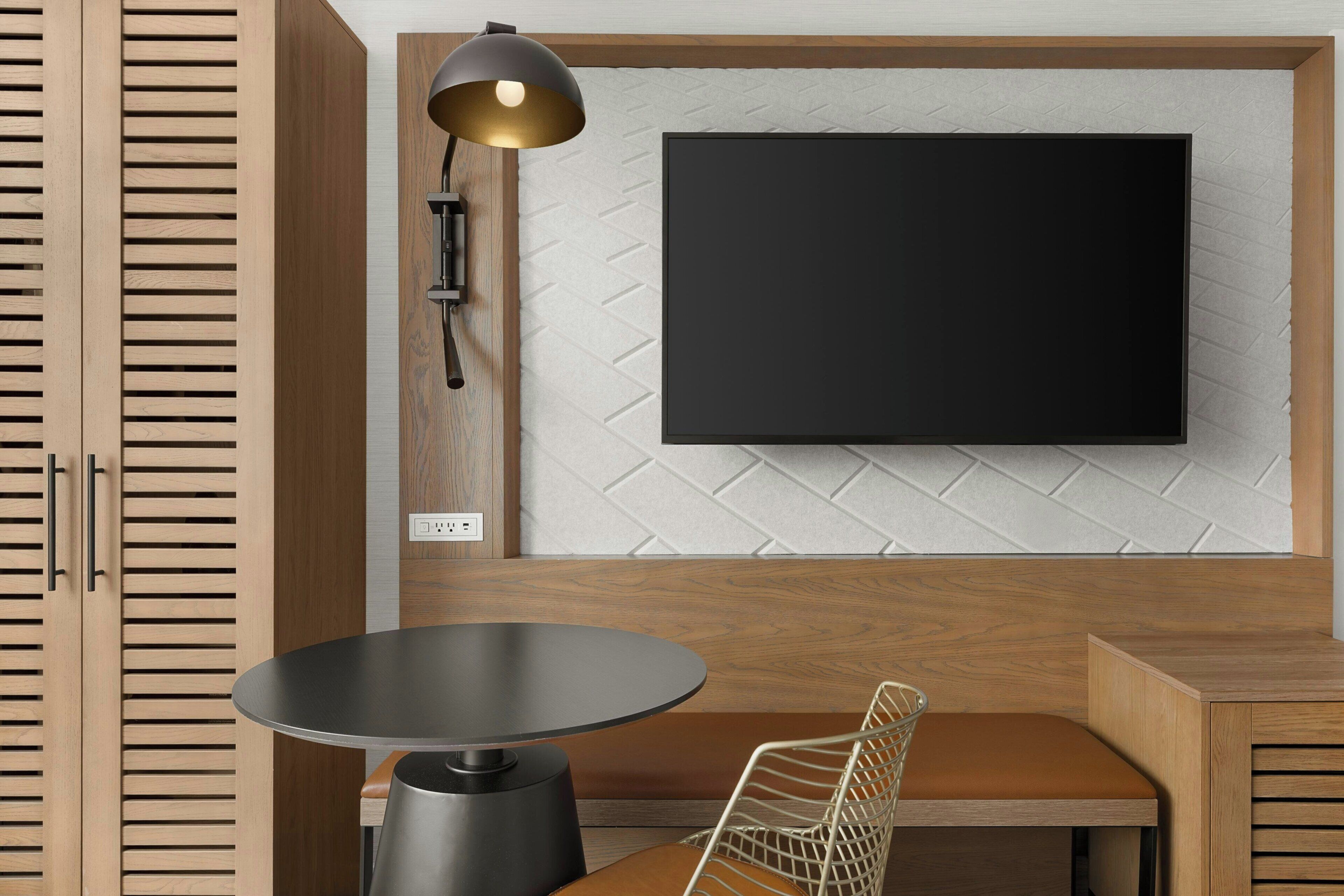 A modern room with a wooden cabinet, a round table, a chair, a wall-mounted TV, and a floor lamp.
