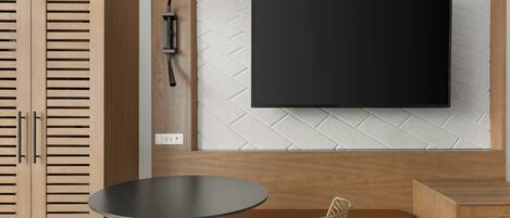 Une pièce moderne avec un meuble en bois, une table ronde, une chaise, un téléviseur fixé au mur et un lampadaire.