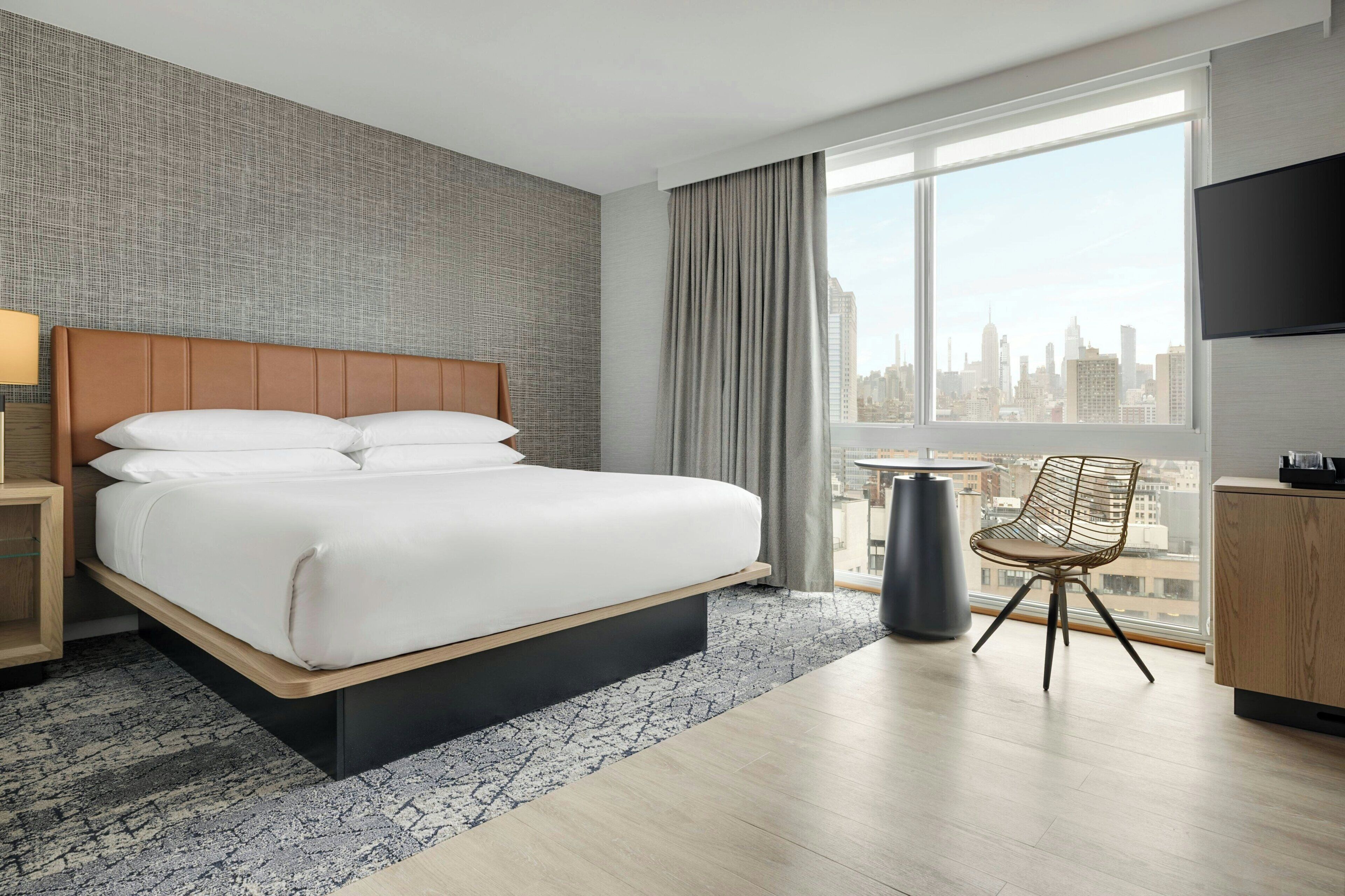 Hotelkamer met een groot bed, een stoel, een televisie en uitzicht over de stad.