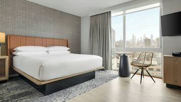 A hotel room with a large bed, a chair, a TV, and a city view.