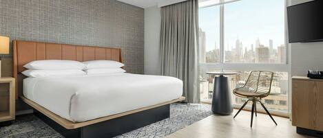 Ein Hotelzimmer mit einem großen Bett, einem Sessel, einem Fernseher und Blick auf die Stadt.