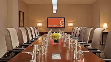 Un salón de conferencias con una larga mesa, sillas y una pantalla que muestra 'Sheraton Tribeca'.