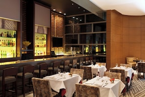 Un ristorante con diversi tavoli e sedie, una zona bar con bottiglie e un'ampia vetrata con vista.