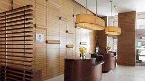 Een receptiegedeelte met een houten wand, een receptiebalie en twee hanglampen.
