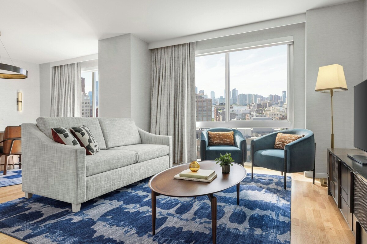 Una sala moderna con sofá, sillón, mesa de centro y vistas a la ciudad.