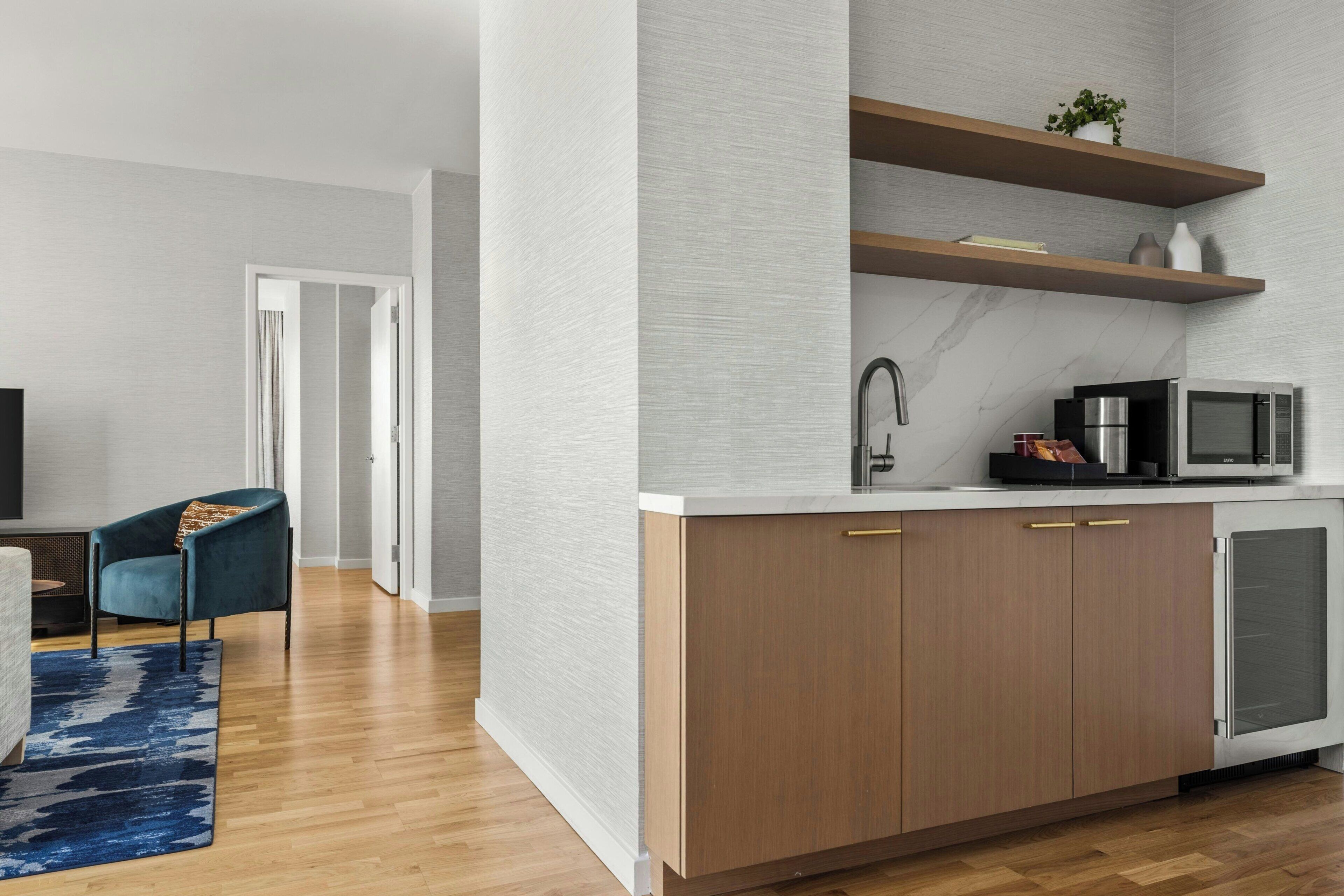 A modern kitchen with a microwave, sink, and cabinets. There is a blue chair and a rug in the living area.
