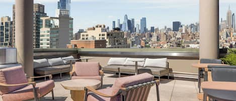 Terraza en la azotea con mobiliario, incluyendo sofás y sillones, y vistas a un horizonte urbano.