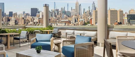 A rooftop terrace with outdoor seating, a city skyline view, and a modern urban environment.