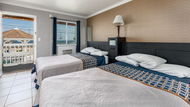 A hotel room with two beds, a nightstand, a lamp, and a view of the sea. - Boardwalk Hotel Charlee & Beach House Rentals (Seaside Heights)