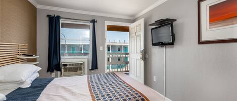 Una habitación de hotel con cama, televisión, balcón y vistas a otros edificios.