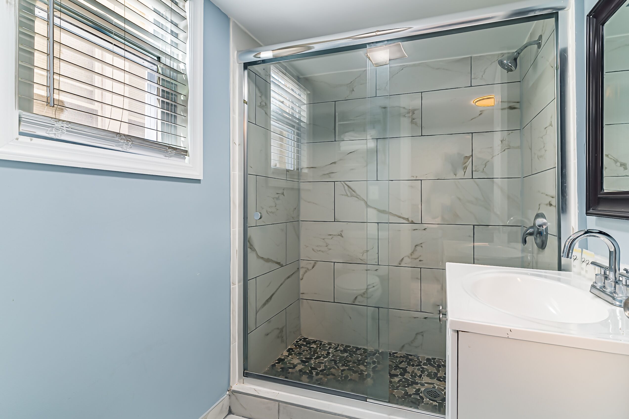 A bathroom with a glass-enclosed shower, a white sink, and a mirror.