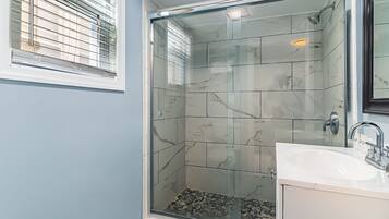 A bathroom with a glass-enclosed shower, a white sink, and a mirror.