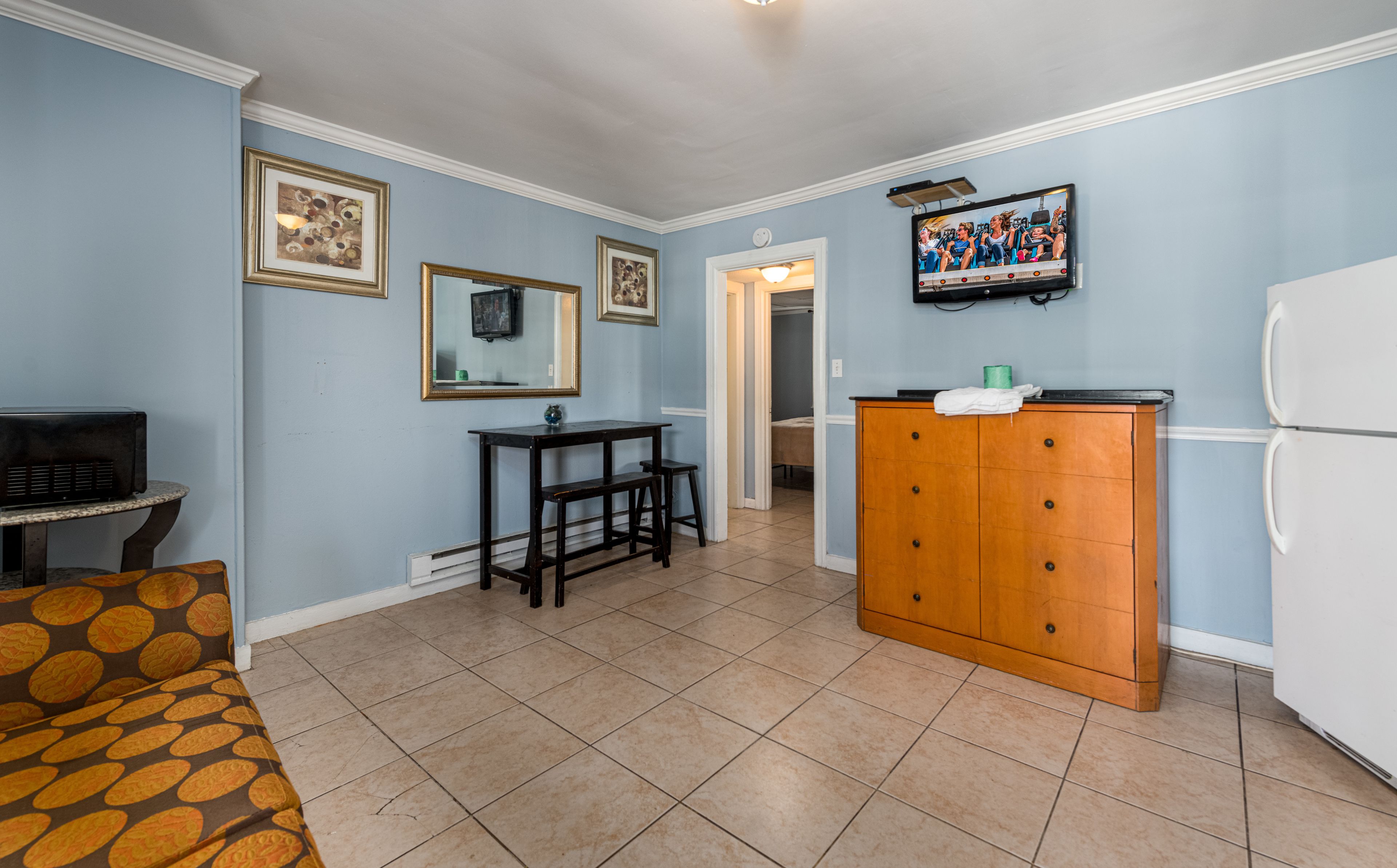 A room with a dining table, chairs, a refrigerator, a wooden cabinet, and a television mounted on the wall.