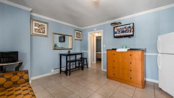 A room with a dining table, chairs, a refrigerator, a wooden cabinet, and a television mounted on the wall.