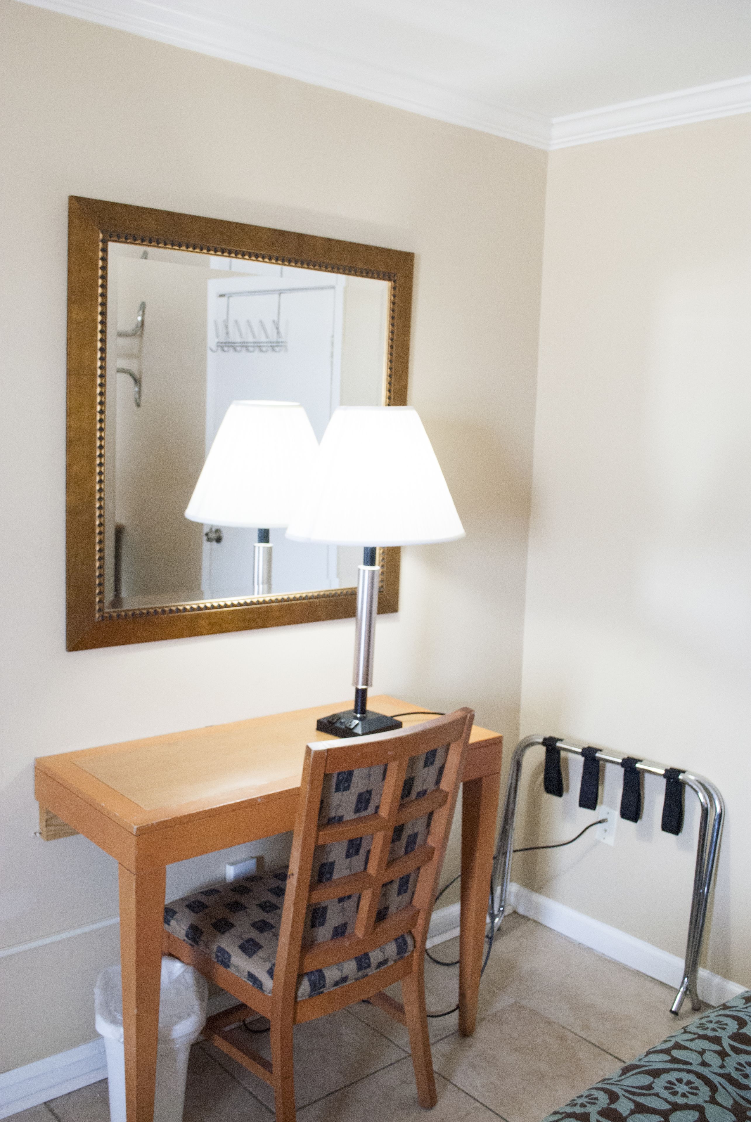 Una habitación pequeña con un escritorio de madera, dos lámparas, una silla y un espejo.