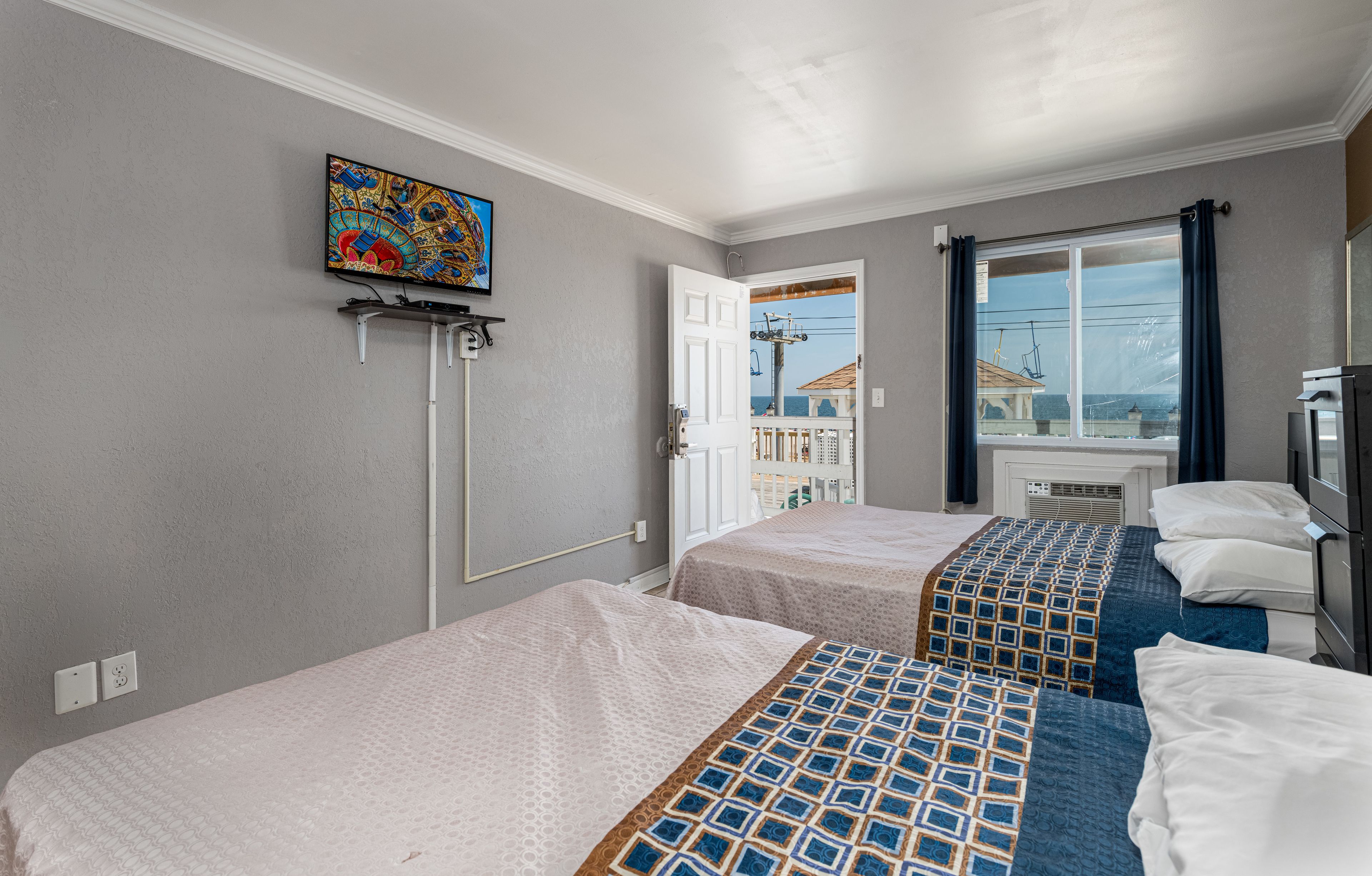 A hotel room with two beds, a TV mounted on the wall, a window with curtains, and a view of the outside.