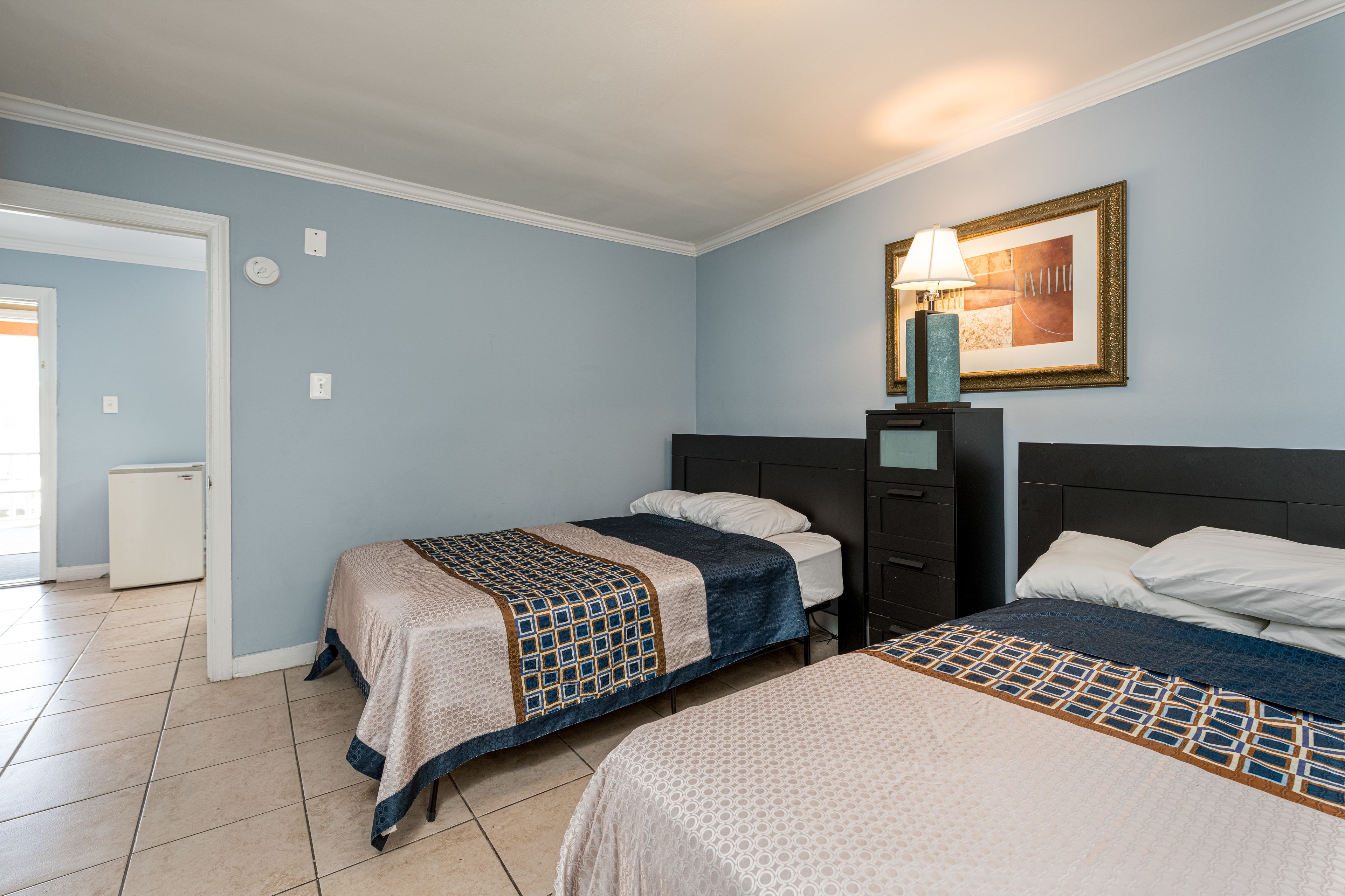 Habitación de hotel con dos camas, una mesita de noche, una lámpara y un cuadro en la pared.