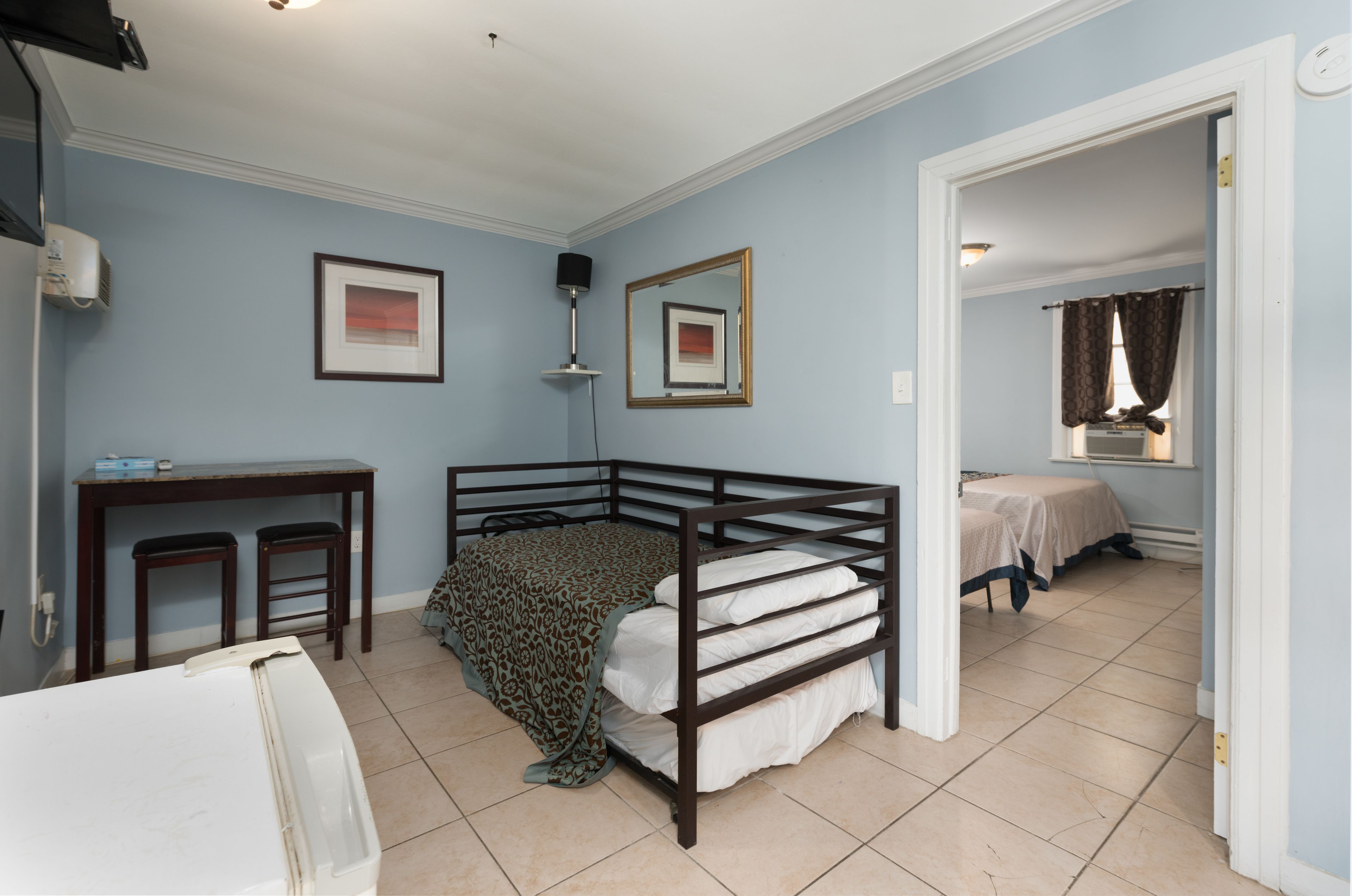 A bedroom with a bunk bed, a desk with two chairs, a mirror, and a window with curtains.