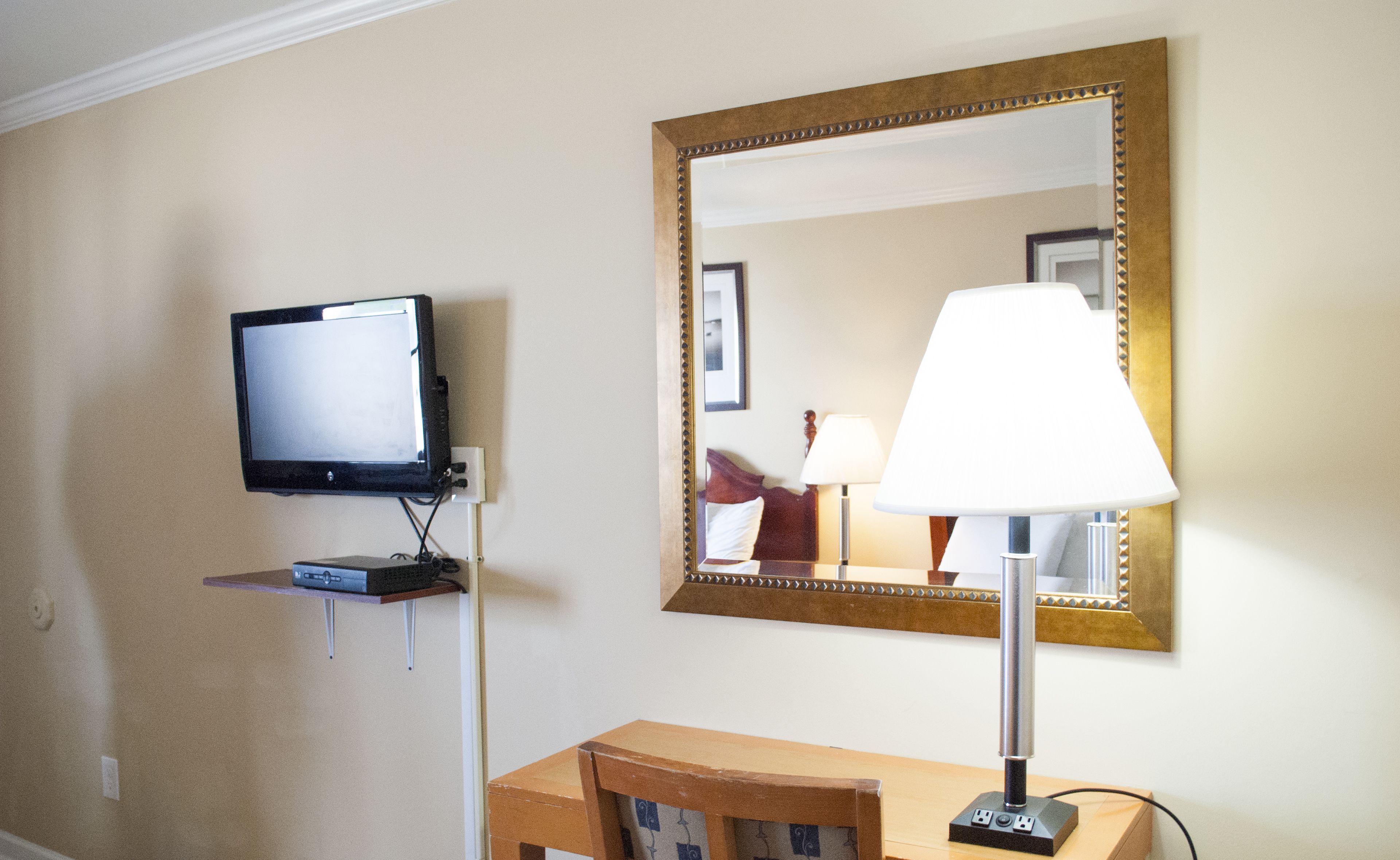 Une chambre d’hôtel équipée d’un téléviseur fixé au mur, d’un bureau avec une lampe et d’un grand miroir.