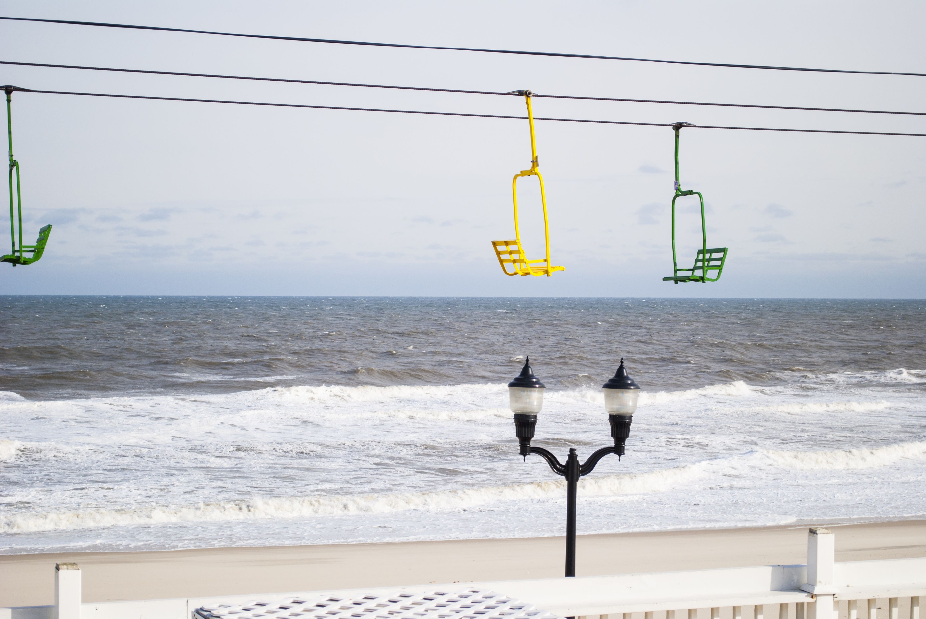 Vista sul mare con un corrimano, un lampione e una sedia sospesa da un cavo.