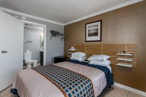 Um quarto com cama, mesa de cabeceira, espelho, porta-toalhas e um quadro na parede.