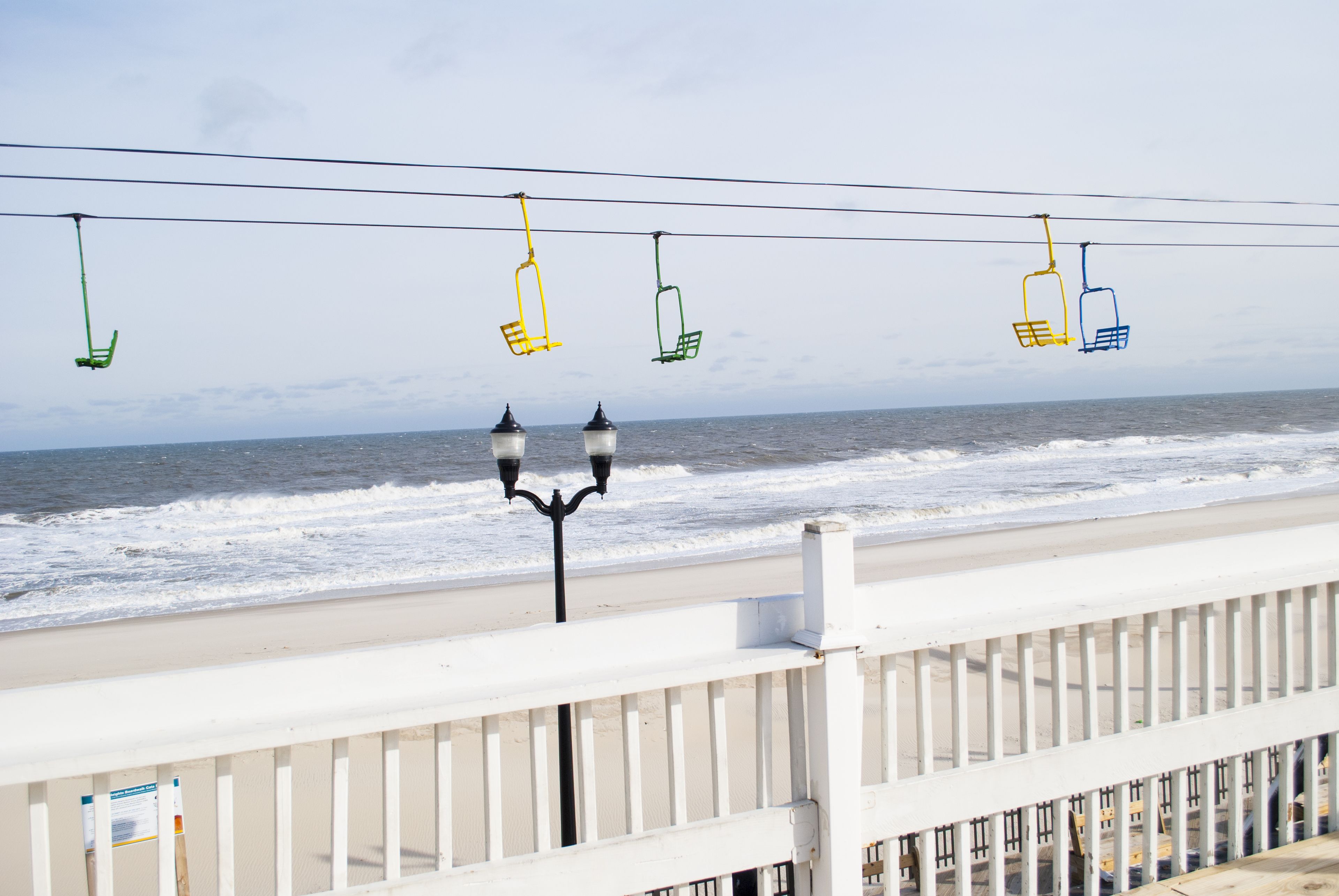 A beach view with a white railing, a lamp post, and colorful chairs suspended over the water.
