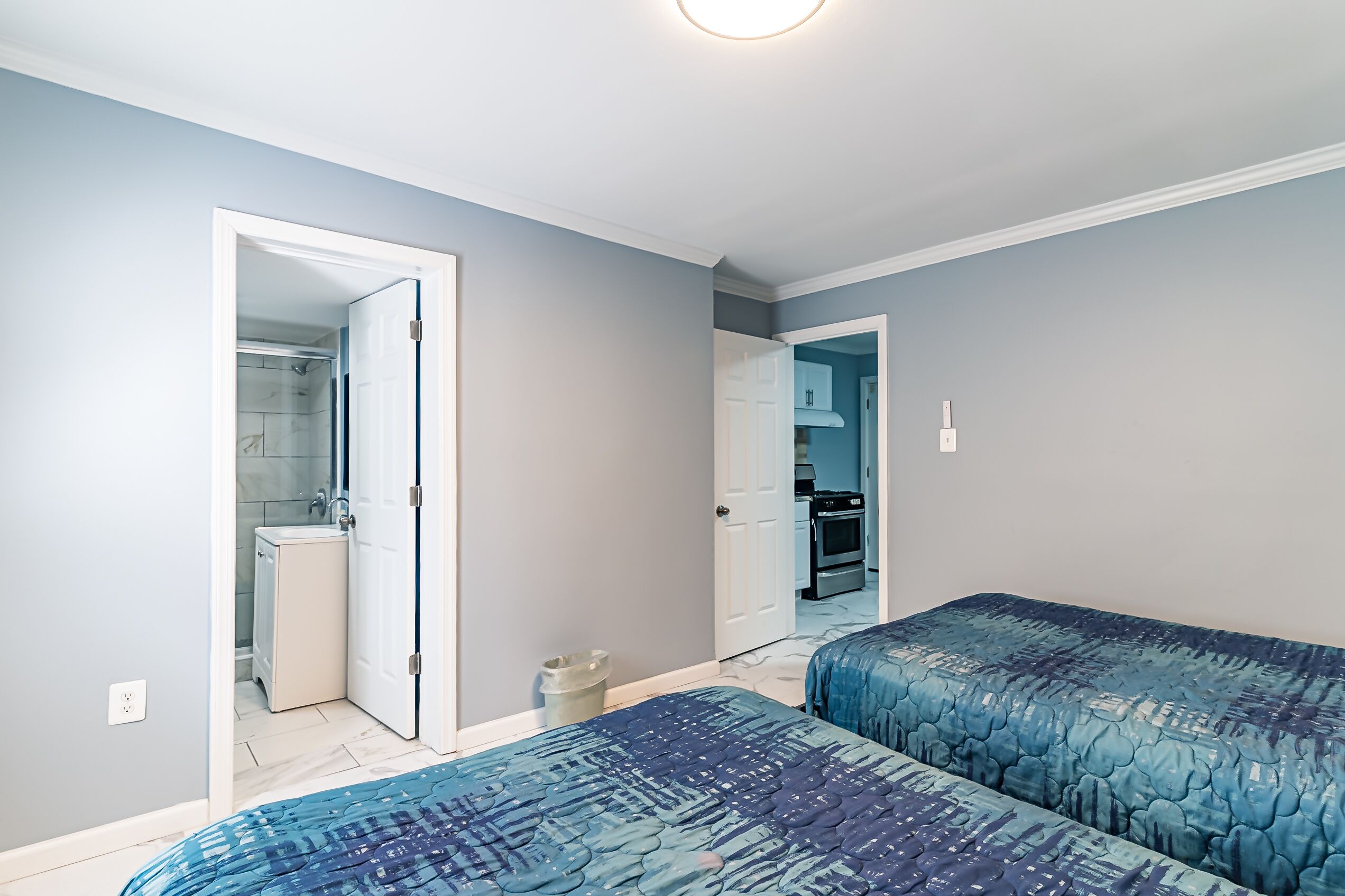 A bedroom with two beds, a bathroom, and a kitchen visible through an open door.