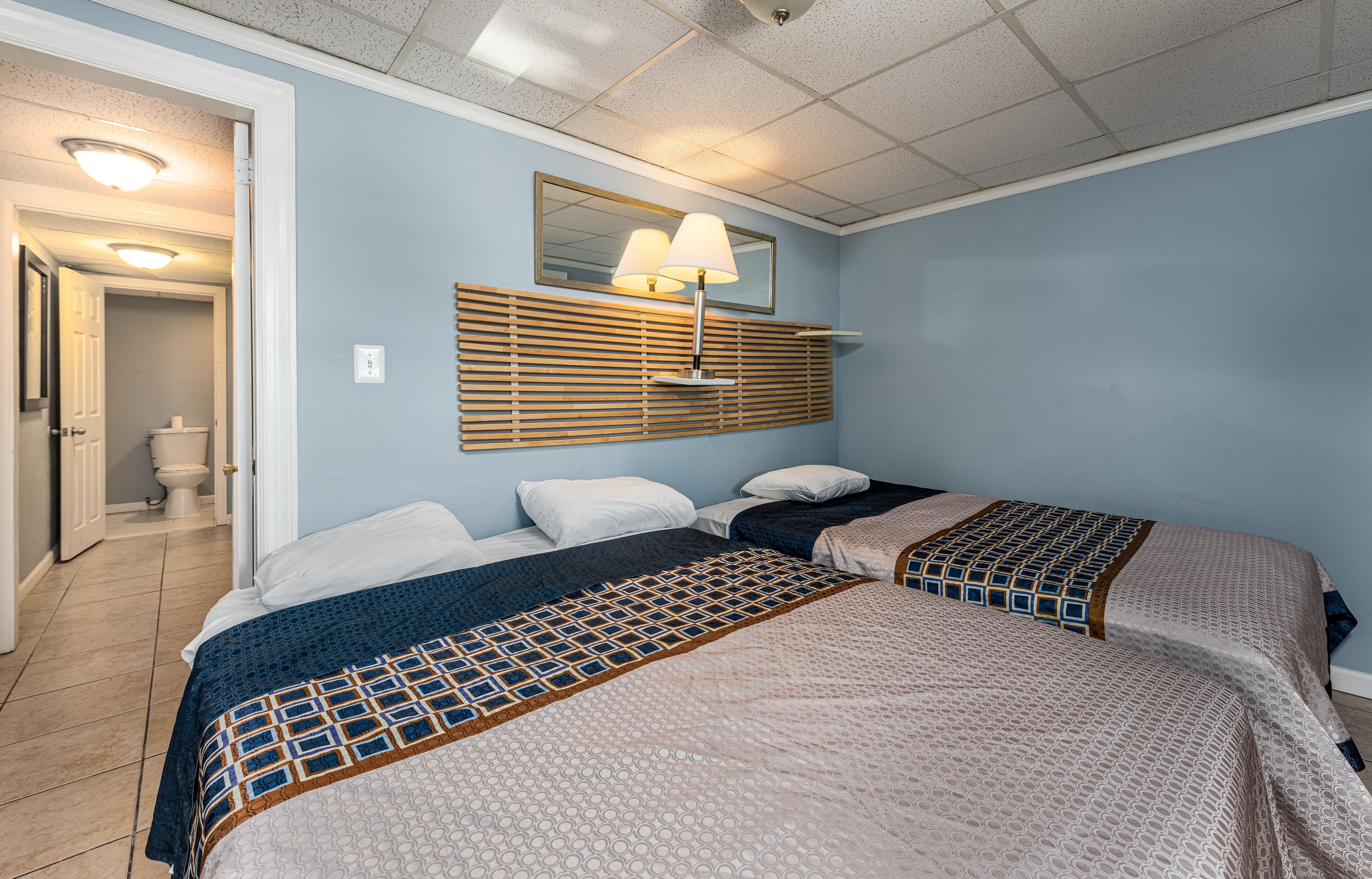 A hotel room with two beds, a mirror, and a ceiling light.