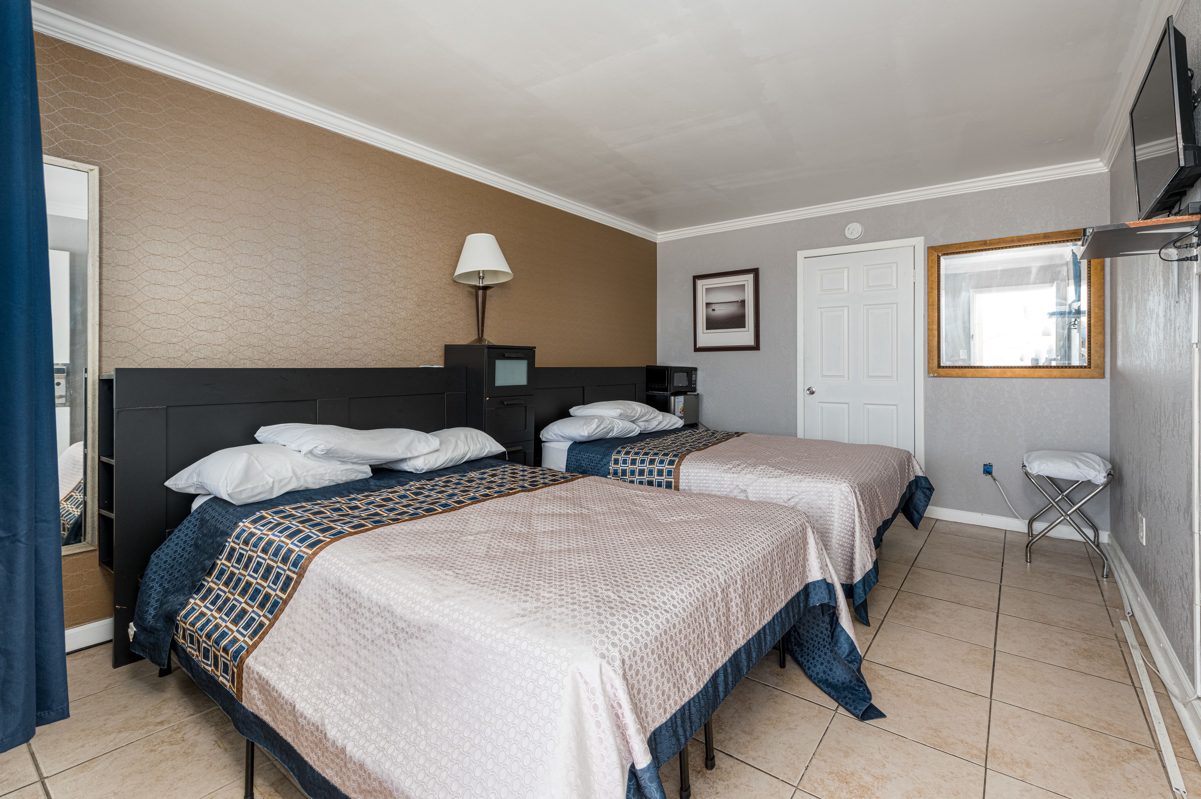 Habitación de hotel con dos camas, un escritorio, una lámpara, un televisor y una ventana.